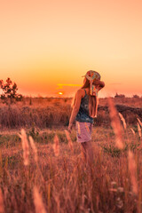 Fototapeta premium A girl stands in a field and looks at the sunset. Summer vacations and rest in the village
