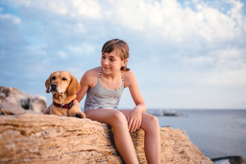 Fototapeta na wymiar Girl embracing her dog while sitting on the rock by the sea
