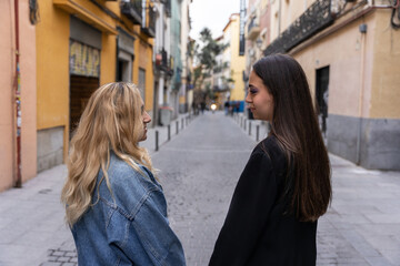 Fototapeta premium Two girls are smiling at each other eyes while having a walk around the city center