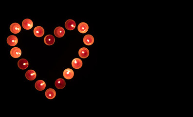 Red burning candles in the shape of a heart on a black background.