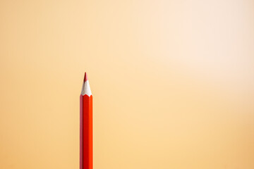 A simple red pencil with a bright orange background, space for text. Top view.