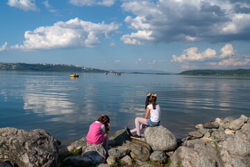 Fototapeta na wymiar Back view of two girls sitting on the shore.