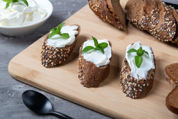 Home made bread on a wooden cutting board with curd cheese and ricotta and herbs. Decorated with...
