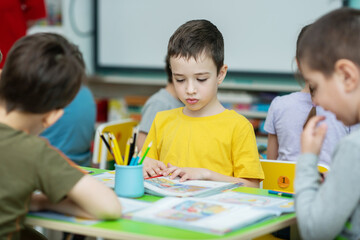 Fototapeta premium The boy preschooler learns to read sitting at the desk with other children. Preparation for school
