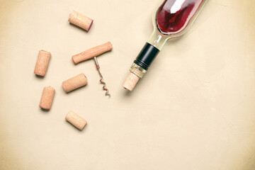 Flat lay incomplete bottle of red wine with cork and corkscrew on beige concrete background. Top view.