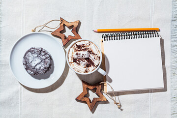 Christmas or New Year festive background. Hot chocolate or cocoa with marshmallow in white cup, chocolate cookies, notebook, copy space,  top view, white background.