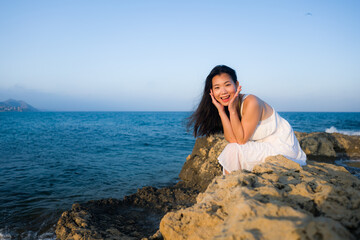 Fototapeta na wymiar holidays lifestyle portrait of young Asian woman by the sea - happy and beautiful Korean girl enjoying beach vacation trip relaxed and cheerful at beach rock cliff