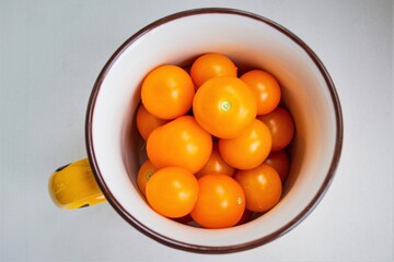 Yellow cherry tomatoes in an iron enamel mug, top view. The focus is on the vegetables and is blurred at the edges of the cup