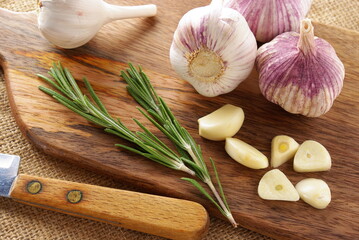 Fresh garlic on a wooden board with rosemary and a knife