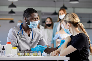 African male Doctor vaccinating cute female,side view. People vaccination concept. Syringe with...