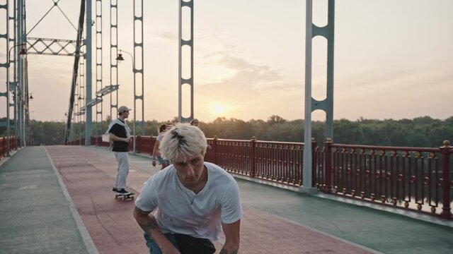 Portrait of a young blond male skater with tattoos and a bright appearance riding on the city bridge at dawn. Freedom and hobby concept