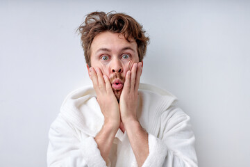 funny guy in bathrobe touching face, in the morning, can't wake up. Bearded male before work, having surprised facial expression. Copy space. Portrait. Isolated white background. Morning routine