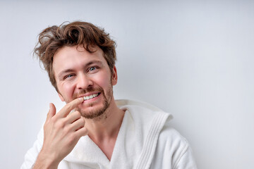 Caucasian young man looking at camera checking is mouth and teeth in bathroom, checking their health state. Handsome guy in the morning after taking bath, copy space. Prthodontics, people lifestyle