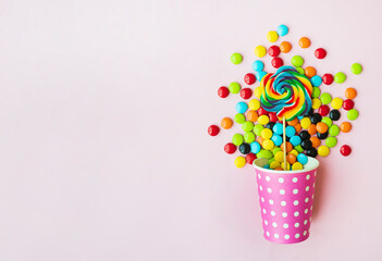 Paper cup with tasty candies on color background
