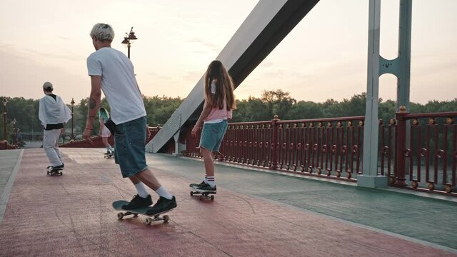 Group of skaters, boys and girls, ride their skateboards across the large city bridge at dawn. Youth culture and freedom of expression concept