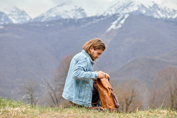 Side view portrait of handsome caucasian male opening backpack in nature, take a break during adventure in mountains, alone, male have rest. travel, people lifestyle concept