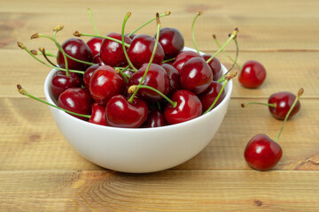 Delicious sweet cherry berries in a bowl on wooden table.