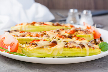 Ready-to-eat baked zucchini halves stuffed with cheese and tomato  on a plate on the table. Vegetable menu, healthy food. Close-up
