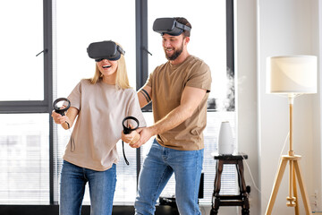 , caucasian couple learning to play video game wearing Visual reality or VR headset playing video console game together in bright cozy living room. fun, leisure, modern technologies