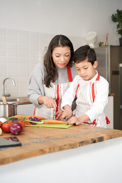 The Child Learns To Cut Vegetables While The Mother Watches And Helps Him Carefully. Latin People Making Typical Latin American Food. Mother And Son Cooking Together.