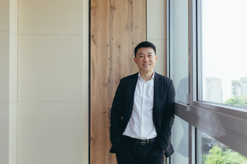 Fototapeta premium Freelancer Asian businessman in business suit looking at camera near the window of a modern office center