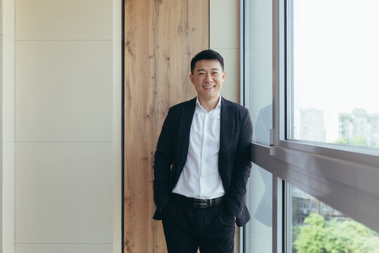 Freelancer Asian businessman in business suit looking at camera near the window of a modern office center
