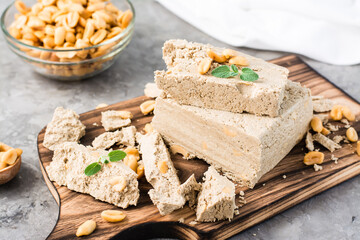 Pieces of sunflower and peanut halva and mint leaves on a cutting board and a bowl of nuts on the table. Caloric oriental dessert. Close-up