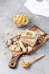 Pieces of sunflower and peanut halva and mint leaves on a cutting board and a bowl of nuts on the table. Caloric oriental dessert. Vertical view