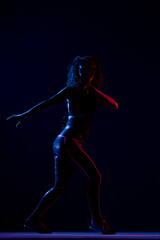 Silhouette of a girl dancing zumba. Side lit with blue and red lights on dark background.