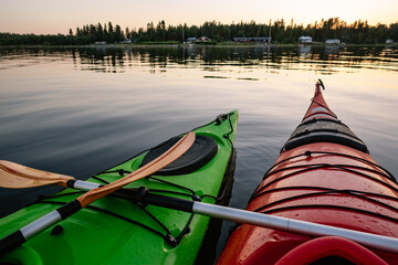 Two green and red wet kayaks float still together on water surface with two crossed orange paddles, summer evening, sea kayaking in Northern Sweden, Umea