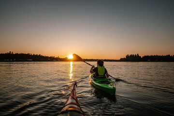 Girl kayaking in calm sea at midnight in Northern Sweden during light Summer nights. All day around Sun in polar regions. - obrazy, fototapety, plakaty