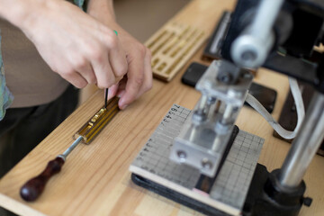 Closeup craftsman hands typing text for branding leather with personal stamp. Creating craft label