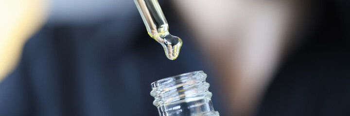 Woman picking up cosmetic oil with pipette from bottle closeup