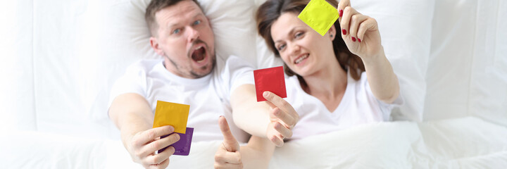 Man and woman lying in bed and holding condoms top view