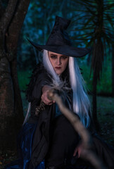 Fototapeta na wymiar Woman in a witch costume in the forest at twilight holding a wooden stick