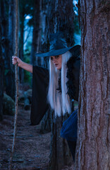 Woman in a witch costume in the forest at twilight holding a wooden stick