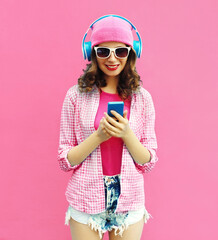 Summer colorful portrait of stylish modern young woman listening to music in headphones with smartphone on pink background