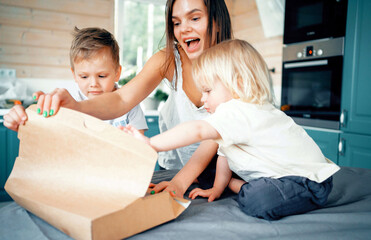 They open a pizza delivery box. Young family mom and two children boys. Play fun games in the...