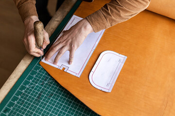 Male tanner making cutting scheme of bag working at leather workshop. Handcrafted creating - obrazy, fototapety, plakaty