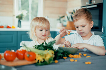 Play together with friends and brothers. Boys children eat colored vegetables in the kitchen from a plate. Happy time happy mood.
