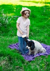 Fototapeta premium a small, beautiful girl in a hat, combing her dog, in the park on a blanket and green grass
