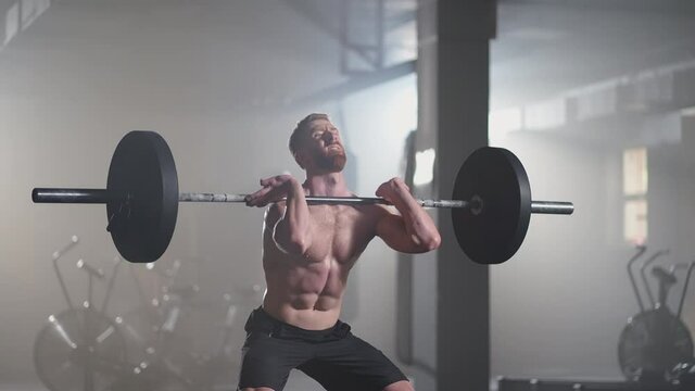 Slow motion: fitness man bodybuilder training using barbell weightlifting exercise muscular sportsman power lifting heavy weight doing squats in gym practice enjoying healthy lifestyle