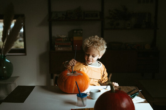 Blond child painting a pumpkin