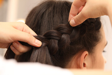 Naklejka premium Professional stylist braiding client's hair on blurred background, closeup