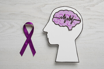 Human head cutout with brain, pulse line and purple ribbon on white wooden background, flat lay....