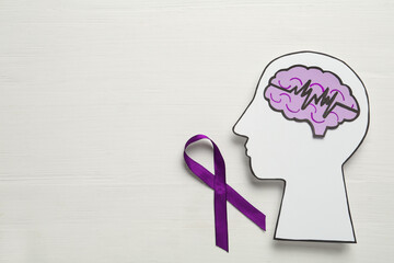 Human head cutout, brain and purple ribbon on white wooden background, flat lay with space for...