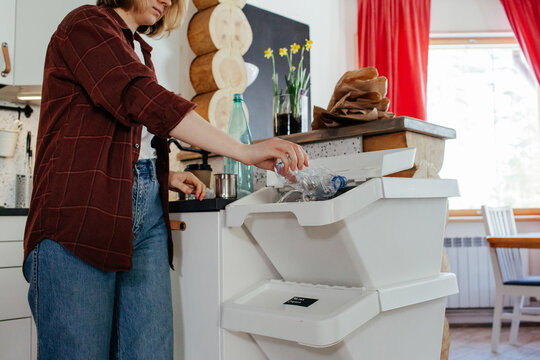 Housewife throwing plastic bottle into trash bin for recycling