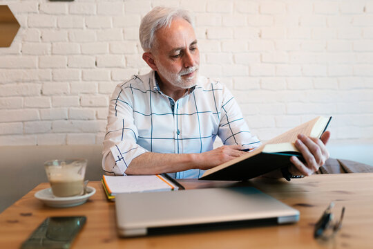 Serious man reading book at table in cafe