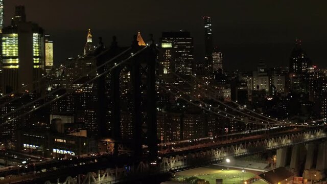 AERIAL: Spectacular drone view of the Manhattan bridge in the middle of the night. Breathtaking heli shot of the bright city lights of New York City at midnight. Cityscape of American metropolis.