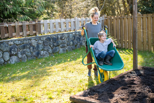 Mother and son play with a wheelbarrow in their back yard.